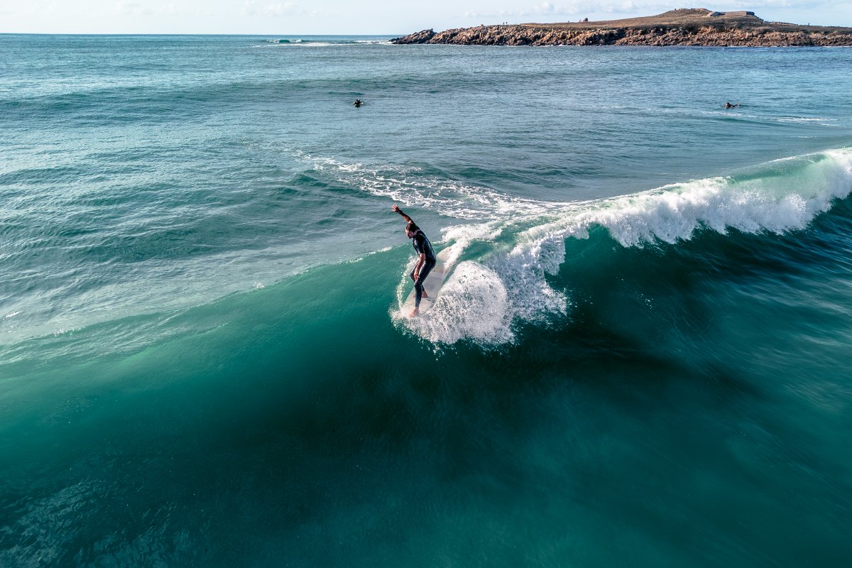 Surfer riding a wave in the ocean with cliffs in the background at LA Torche in FRANCE with a classic surfboards of SIC MAUI