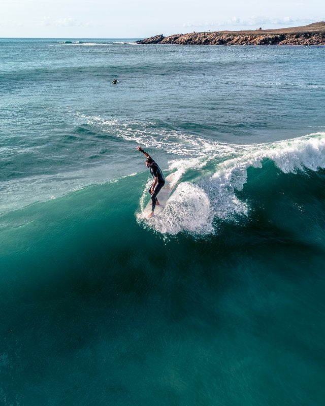 Surfer riding a wave in the ocean with cliffs in the background at LA Torche in FRANCE with a classic surfboards of SIC MAUI