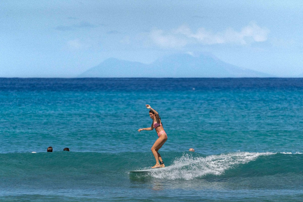 Person surfing on a wave with mountains in the background, surfgirl with a Smuggler longboard