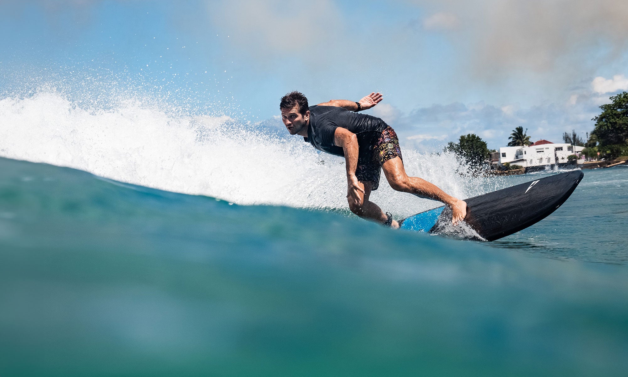 Person surfing on a wave with a clear sky and buildings in the background on his Phantom surfboard by Sicmaui