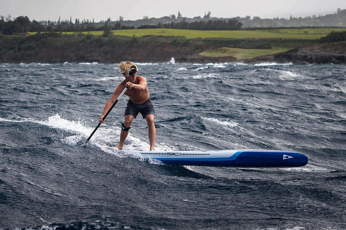 Person paddleboarding on rough water with a scenic background and SIC Maui SUP