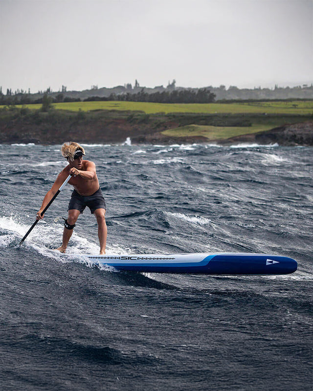 Person paddleboarding on rough water with a scenic background and SIC Maui SUP