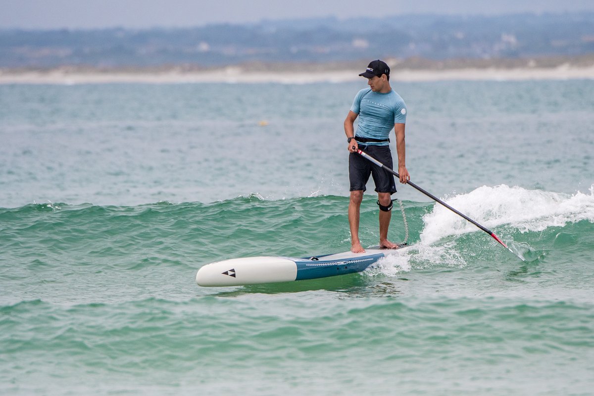 Action shot of a paddler navigating small ocean waves with a versatile SIC Maui all-around paddleboard.