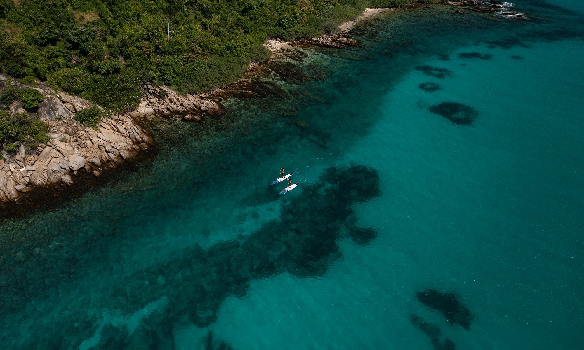 Aerial view of two paddlers exploring a coastline on SIC Maui touring paddleboards in clear turquoise ocean water.