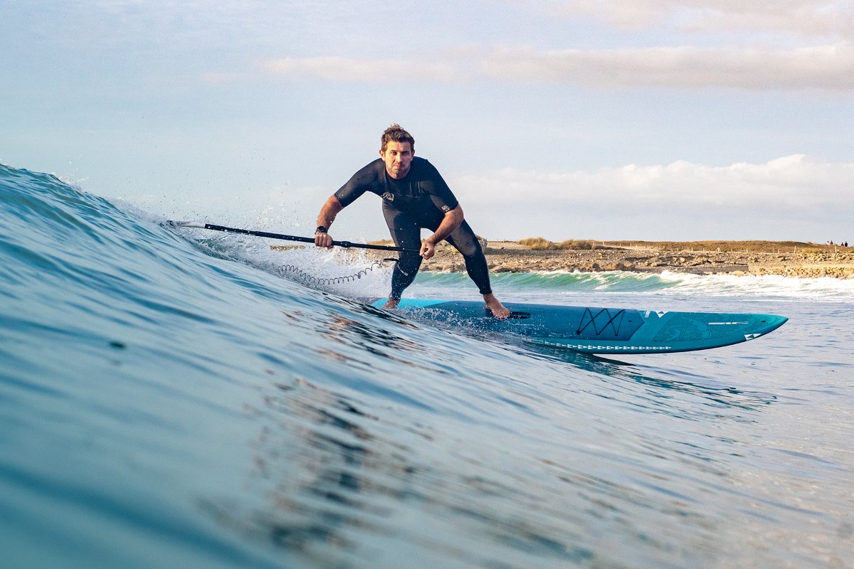 Close-up action shot of a SUP surf session with a paddler executing a turn on a sleek blue SIC Maui all-around paddleboard.
