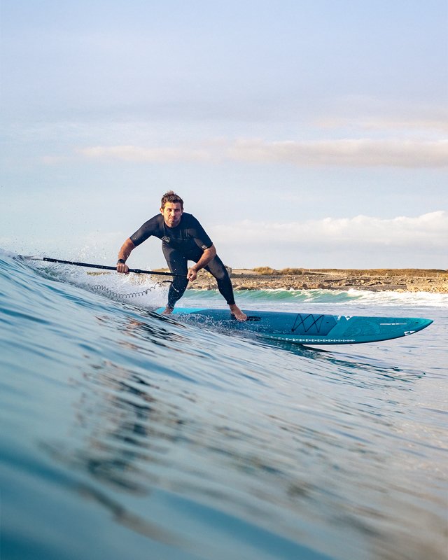 Close-up action shot of a SUP surf session with a paddler executing a turn on a sleek blue SIC Maui all-around paddleboard.
