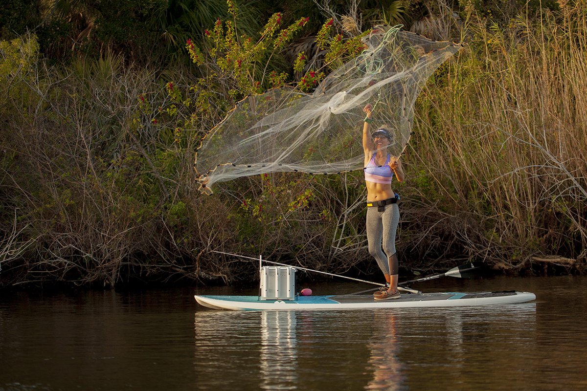 Solo explorer on a versatile SIC Maui all-around paddleboard navigating scenic water near a natural shoreline, demonstrating stability for SUP fishing and long distance paddling.