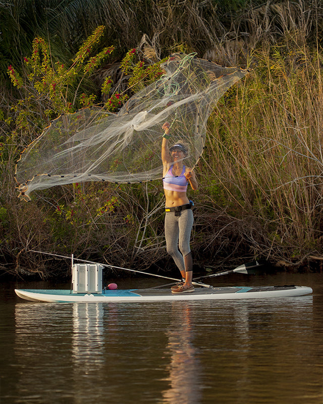 Solo explorer on a versatile SIC Maui all-around paddleboard navigating scenic water near a natural shoreline, demonstrating stability for SUP fishing and long distance paddling.