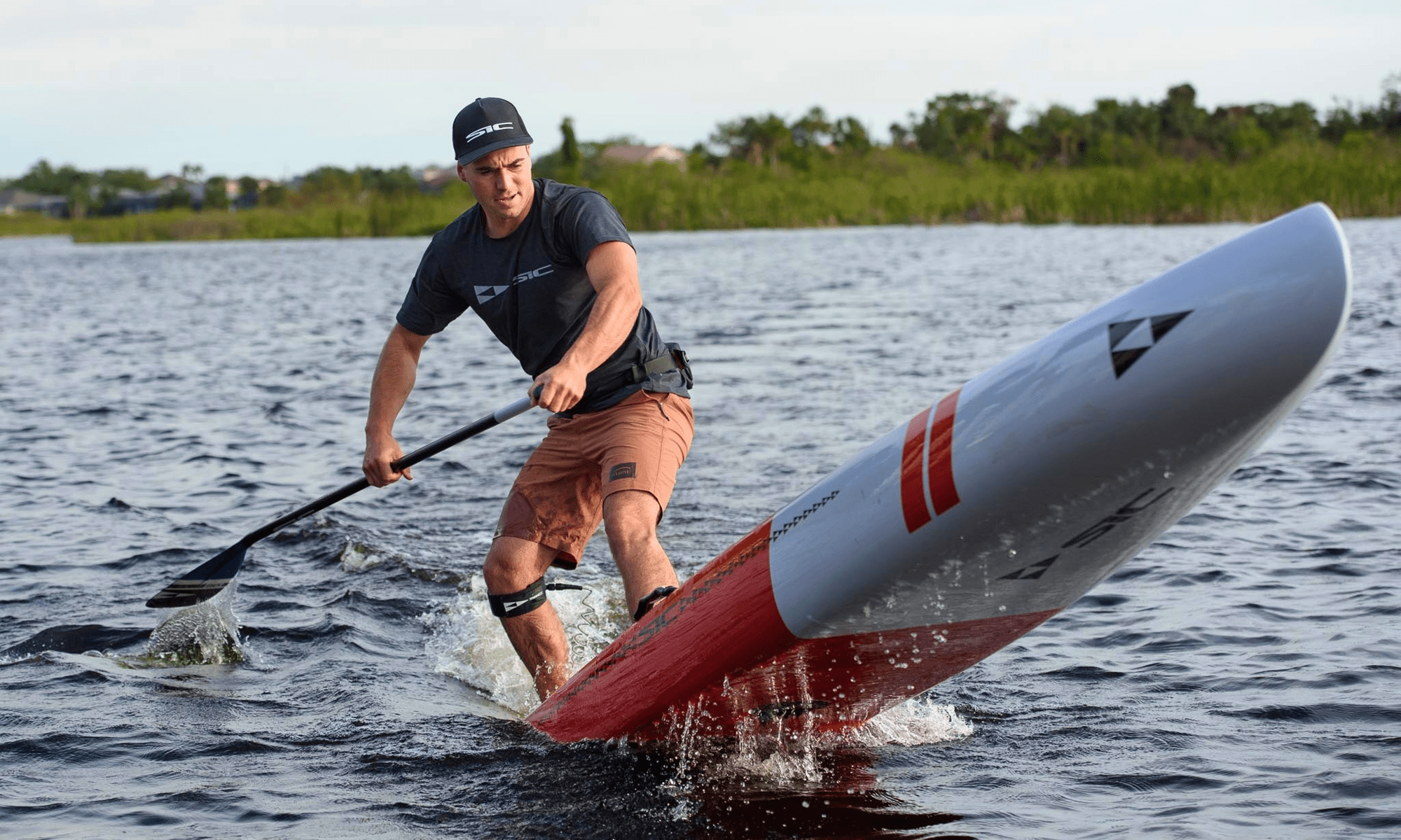 Man paddleboarding on a lake with a red and white SIC Maui race paddleboard