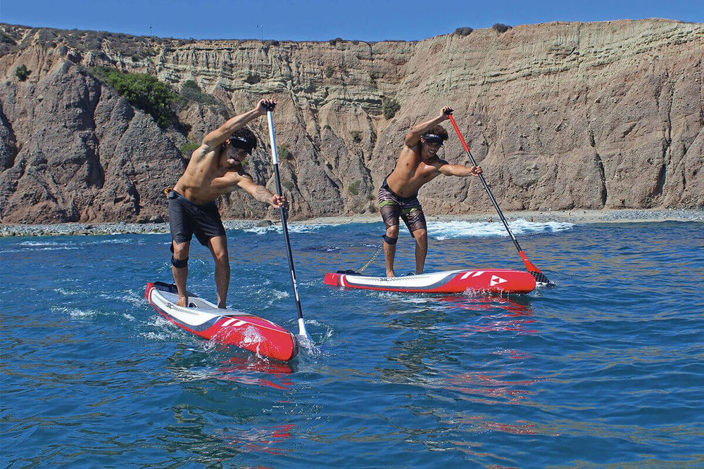Two people paddleboarding on a clear day with cliffs in the background