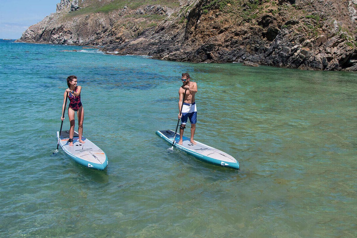 Two people paddleboarding in clear water with rocky cliffs in the background on SIC Maui paddleboards