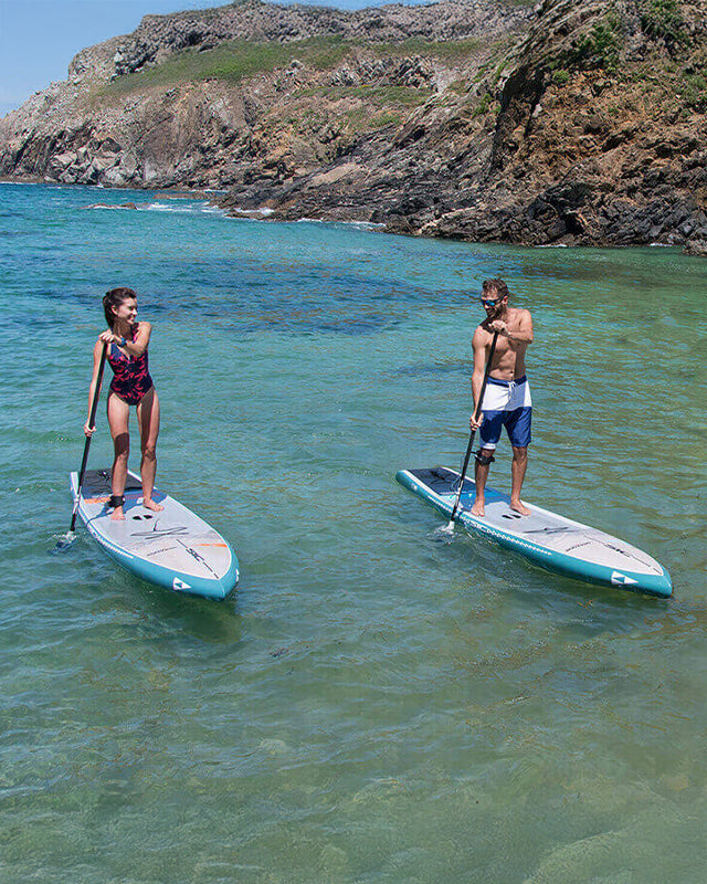 Two people paddleboarding in clear water with rocky cliffs in the background on SIC Maui paddleboards