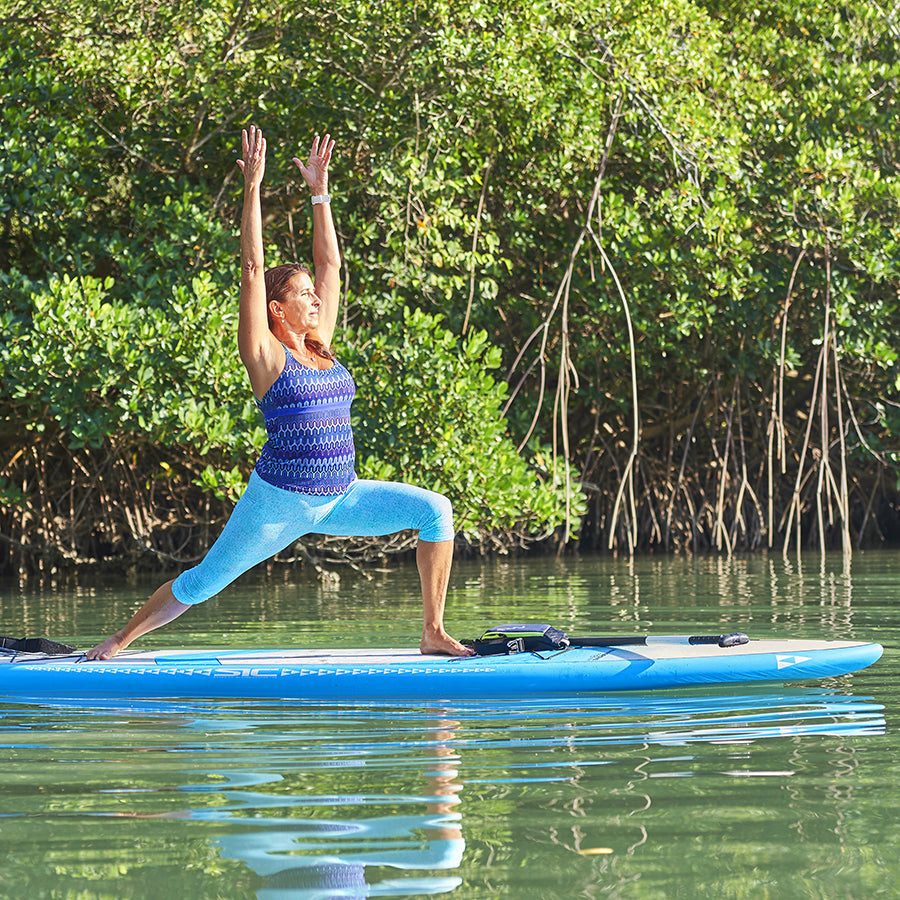 Fitness enthusiast demonstrating balance on a stable SIC Maui inflatable stand up paddleboard in calm waters.