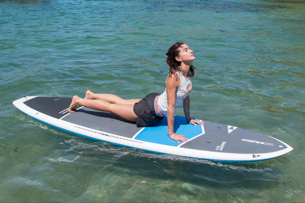 Woman practicing SUP Yoga on a stable SIC Maui Tao Fit stand up paddleboard on calm water.