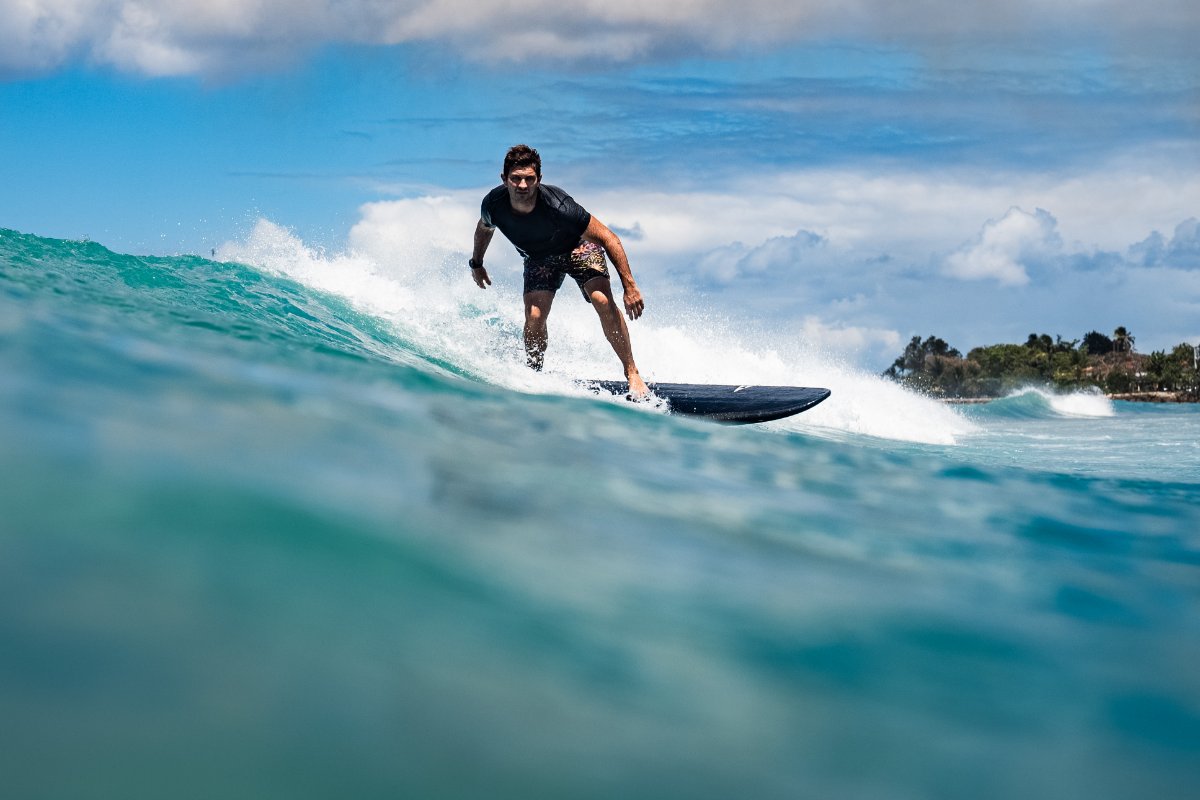 Person surfing on a wave with a clear sky and ocean background with his SIC MAUI Phantom surfboard