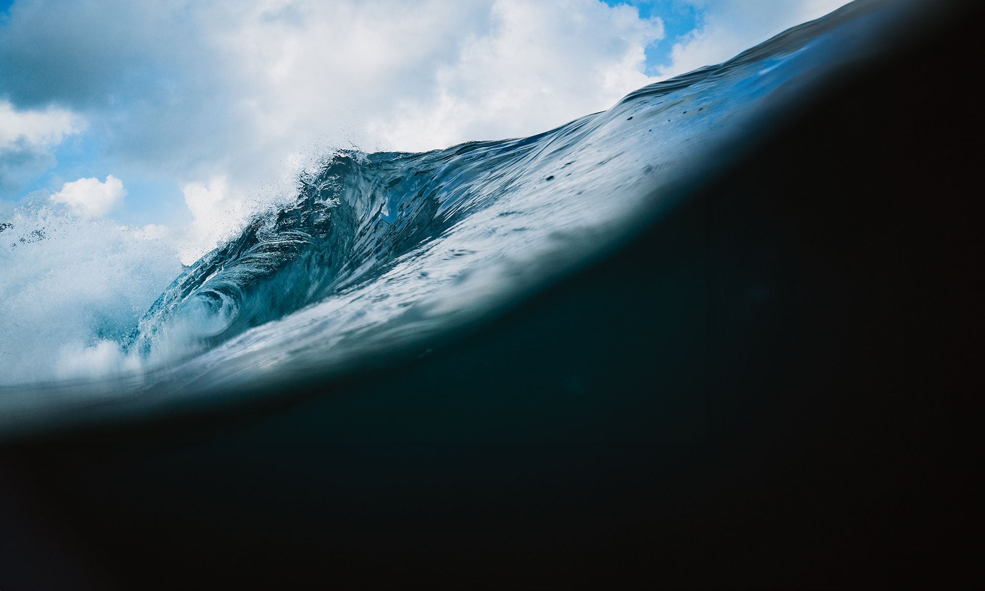 Large wave crashing down with a cloudy sky in the background